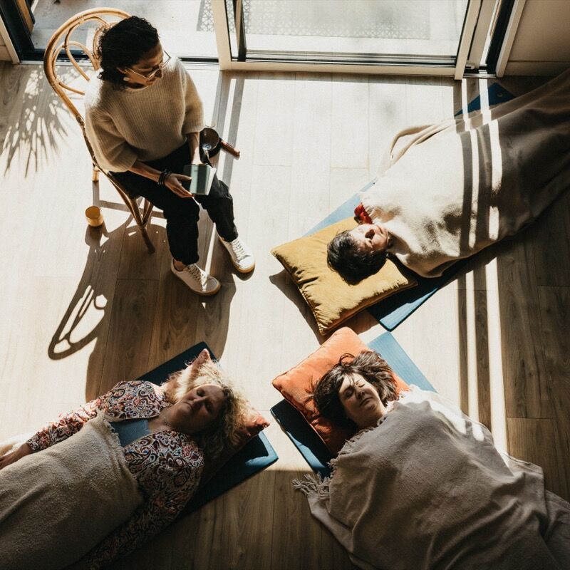 Atelier collectif de relaxation : trois participantes allongées sous des couvertures, Julie Gautier assise auprès d’elles